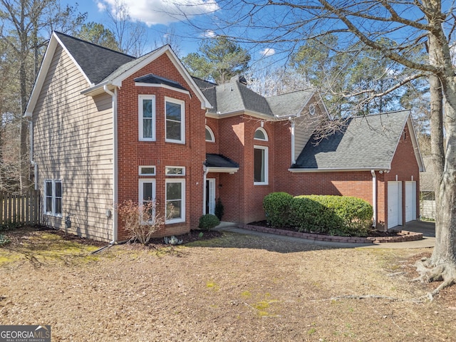 traditional-style house featuring brick siding, a garage, and roof with shingles