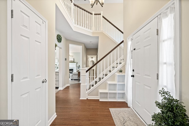 entrance foyer with dark wood-type flooring, stairway, a high ceiling, a fireplace, and baseboards