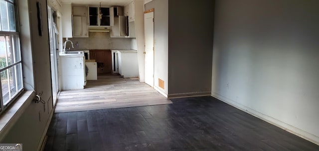 kitchen featuring baseboards, under cabinet range hood, light countertops, wood finished floors, and a sink