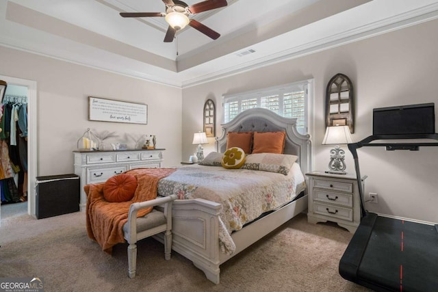 bedroom featuring light carpet, a tray ceiling, a walk in closet, and visible vents