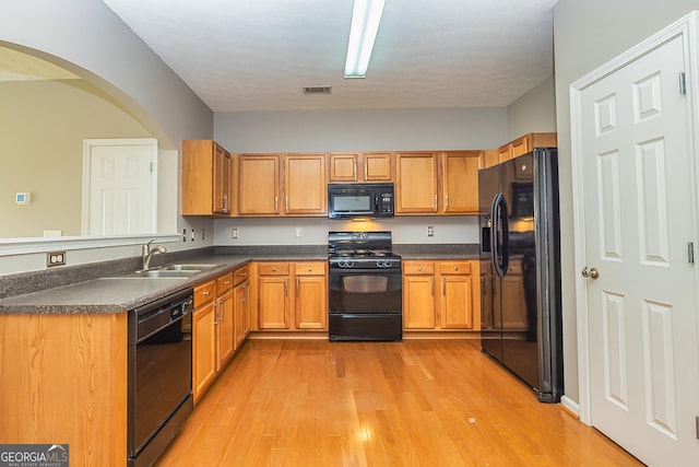 kitchen with a sink, visible vents, black appliances, light wood finished floors, and dark countertops