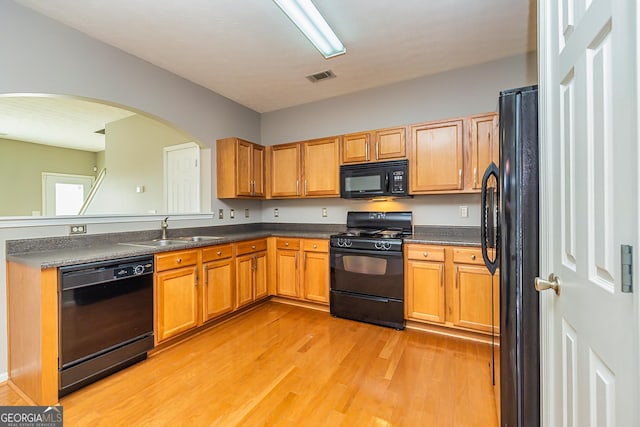 kitchen featuring dark countertops, visible vents, a sink, light wood-type flooring, and black appliances