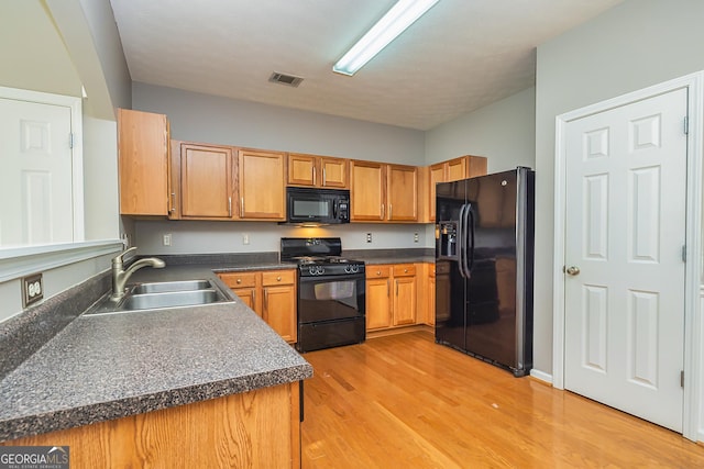 kitchen with light wood-style flooring, a sink, visible vents, black appliances, and dark countertops