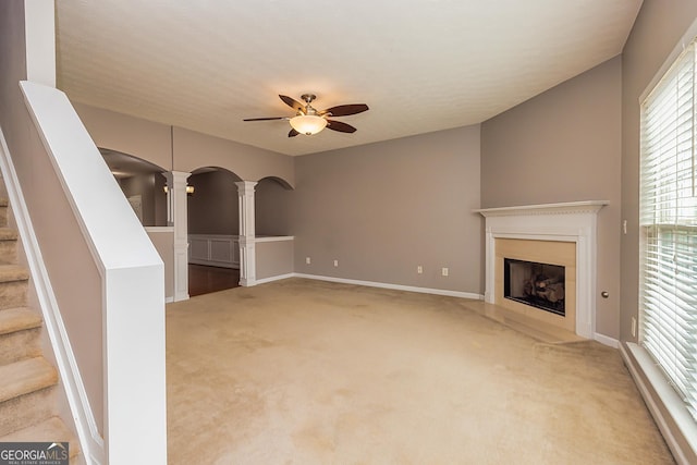 unfurnished living room with arched walkways, stairs, decorative columns, and light colored carpet