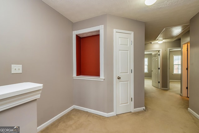 hallway with baseboards, attic access, and light colored carpet