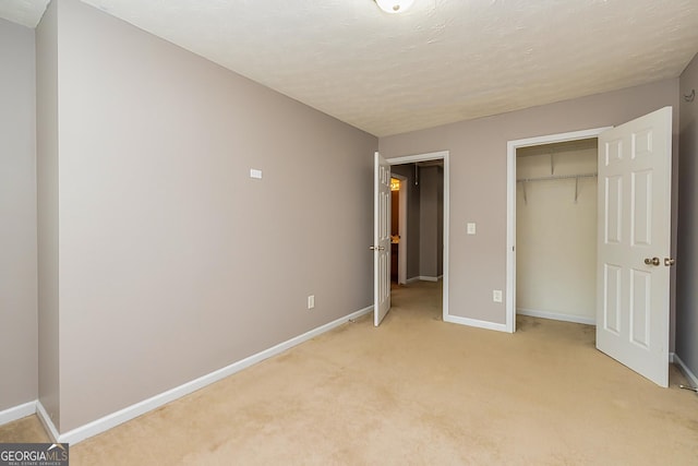 unfurnished bedroom with a closet, light colored carpet, a textured ceiling, and baseboards