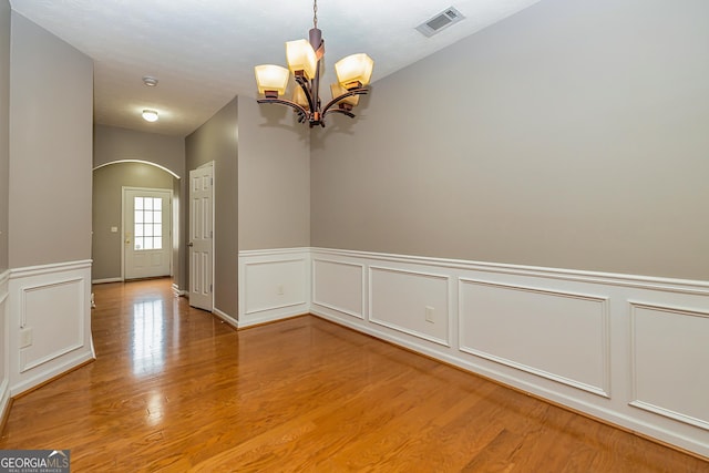 unfurnished dining area with light wood-style floors, a chandelier, visible vents, and a wainscoted wall