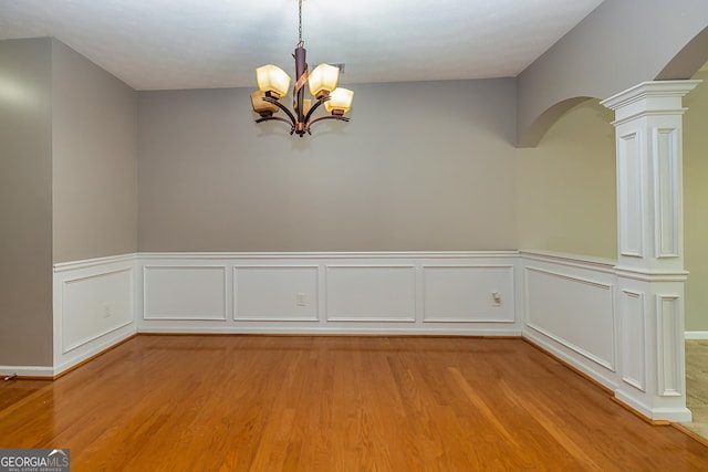 empty room featuring arched walkways, wood finished floors, decorative columns, and an inviting chandelier