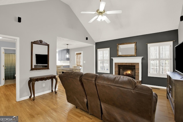 living room with light wood finished floors, a brick fireplace, baseboards, and a ceiling fan