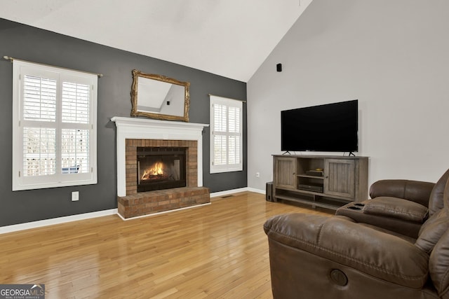 living area featuring light wood finished floors, a fireplace, baseboards, and high vaulted ceiling