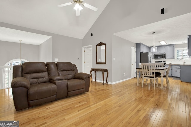 living area featuring high vaulted ceiling, baseboards, ceiling fan, and light wood finished floors