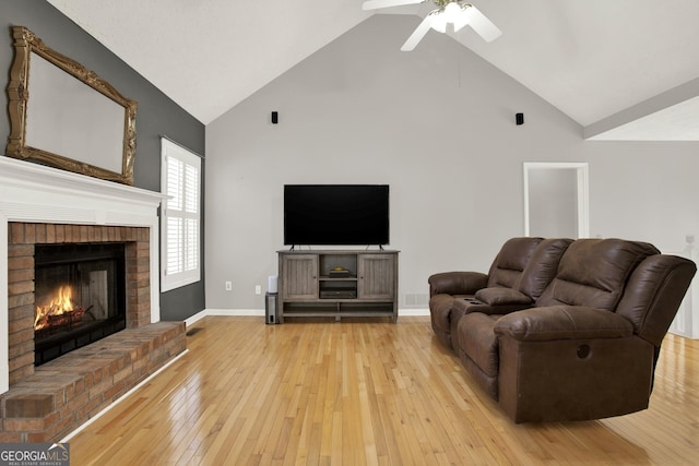 living room featuring high vaulted ceiling, a fireplace, a ceiling fan, baseboards, and light wood-type flooring