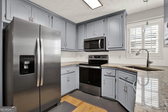 kitchen featuring stainless steel appliances, light wood-type flooring, a sink, and gray cabinetry