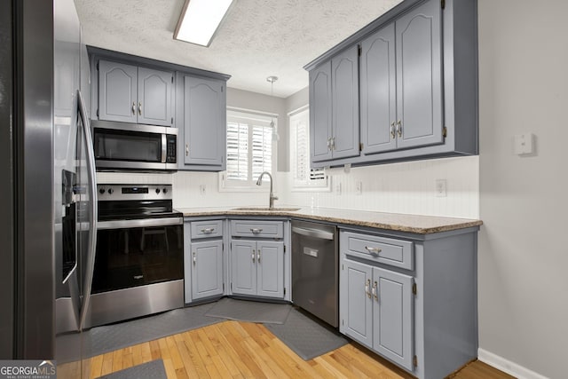 kitchen featuring gray cabinetry, appliances with stainless steel finishes, light wood-style floors, a sink, and a textured ceiling