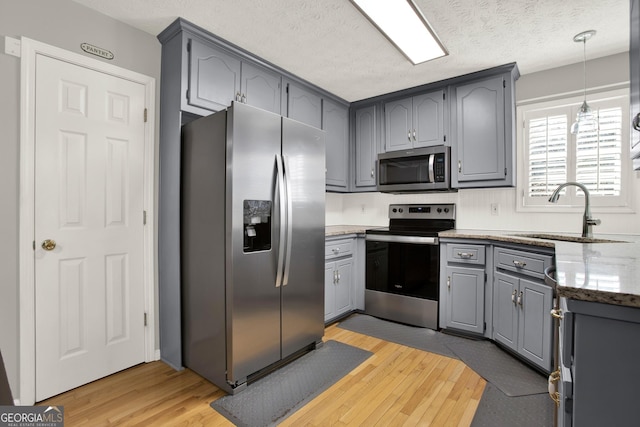 kitchen featuring a sink, appliances with stainless steel finishes, light wood-type flooring, gray cabinets, and light stone countertops