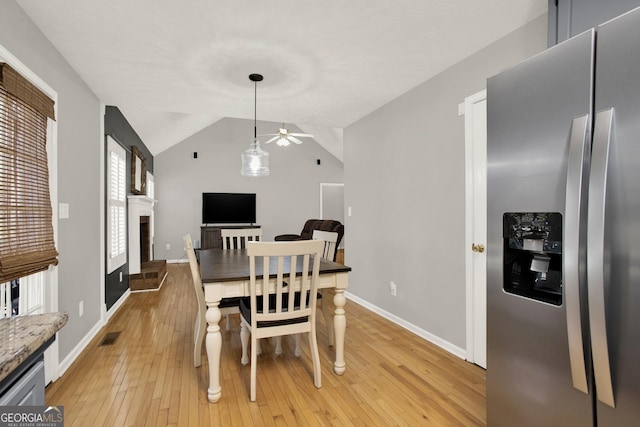 dining room with a fireplace with raised hearth, visible vents, baseboards, vaulted ceiling, and light wood-style floors