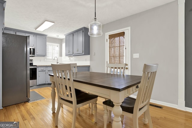 dining area with light wood-style floors, visible vents, baseboards, and a textured ceiling