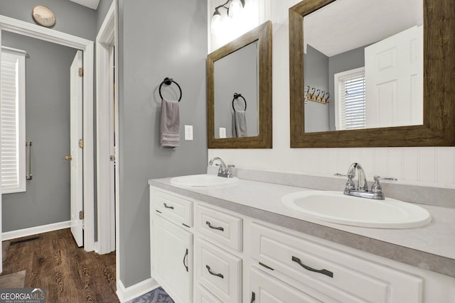 full bathroom with wood finished floors, a sink, baseboards, and double vanity