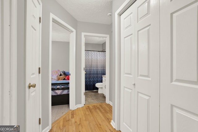 corridor featuring light wood-type flooring, a textured ceiling, and baseboards