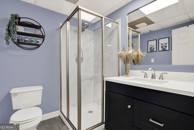 full bathroom featuring a marble finish shower, a drop ceiling, toilet, wood finished floors, and vanity