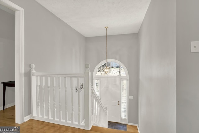 entryway with a notable chandelier, a textured ceiling, baseboards, and wood finished floors