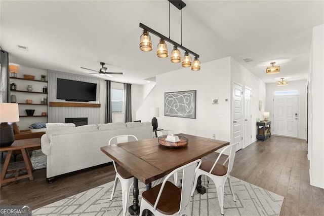 dining area featuring a ceiling fan, a large fireplace, visible vents, and wood finished floors