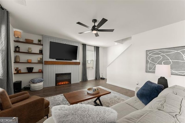 living area featuring a large fireplace, ceiling fan, baseboards, and wood finished floors