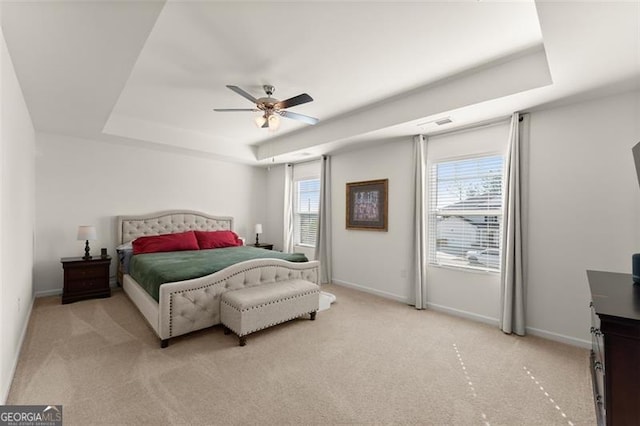 bedroom with light carpet, a raised ceiling, a ceiling fan, and baseboards