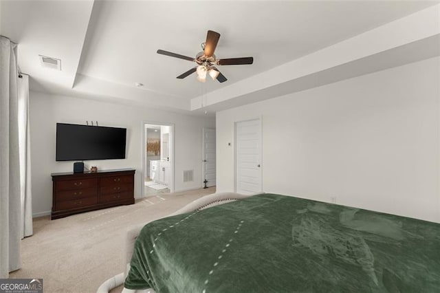 bedroom featuring a tray ceiling, ensuite bath, visible vents, and light colored carpet