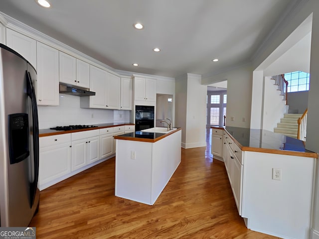 kitchen featuring a kitchen island with sink, under cabinet range hood, white cabinets, black appliances, and tasteful backsplash