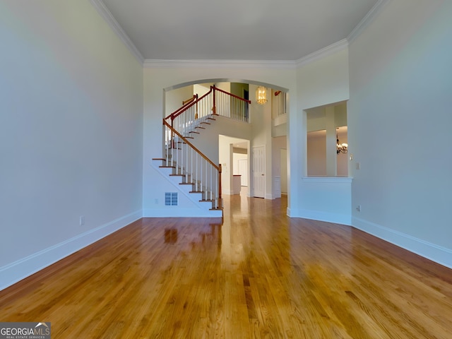 unfurnished living room with a chandelier, wood finished floors, visible vents, baseboards, and ornamental molding