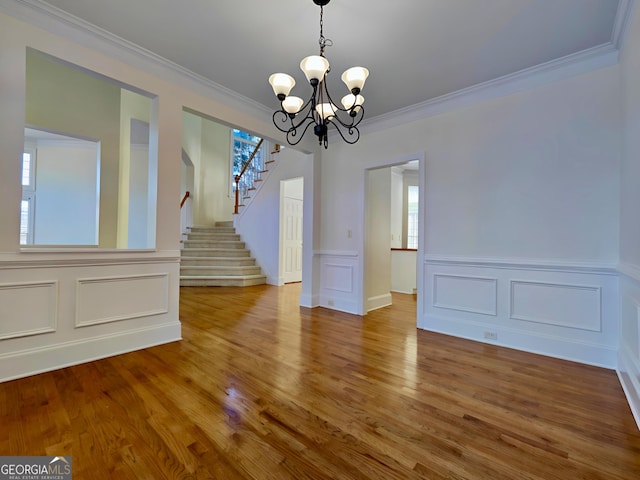 unfurnished dining area featuring stairs, a chandelier, crown molding, and wood finished floors