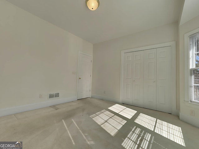 unfurnished bedroom featuring baseboards, a closet, visible vents, and light colored carpet