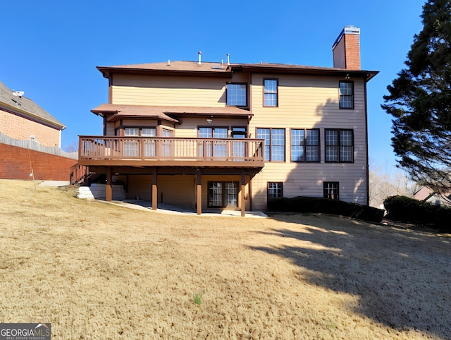 back of property featuring a deck, a chimney, fence, and a lawn