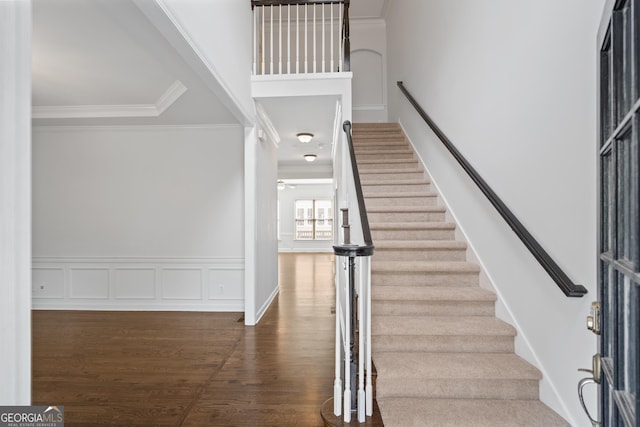 staircase with wainscoting, crown molding, a decorative wall, and wood finished floors