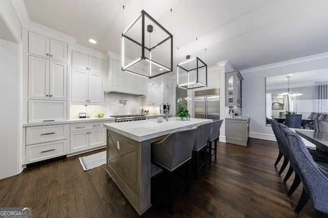 kitchen with a kitchen island with sink, a notable chandelier, dark wood-style flooring, white cabinets, and tasteful backsplash