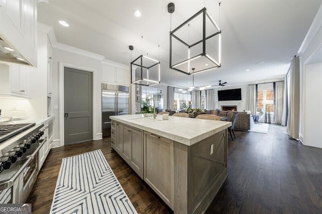 kitchen with built in fridge, open floor plan, a sink, a kitchen island, and a lit fireplace