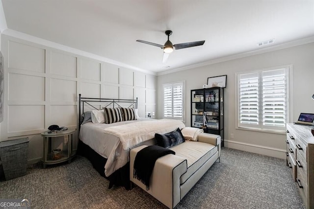 carpeted bedroom with visible vents, baseboards, ceiling fan, ornamental molding, and a decorative wall