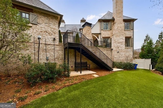 rear view of property featuring brick siding, a patio, a lawn, stairway, and fence