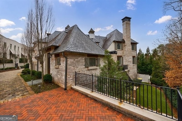 view of property exterior featuring brick siding, a chimney, and fence