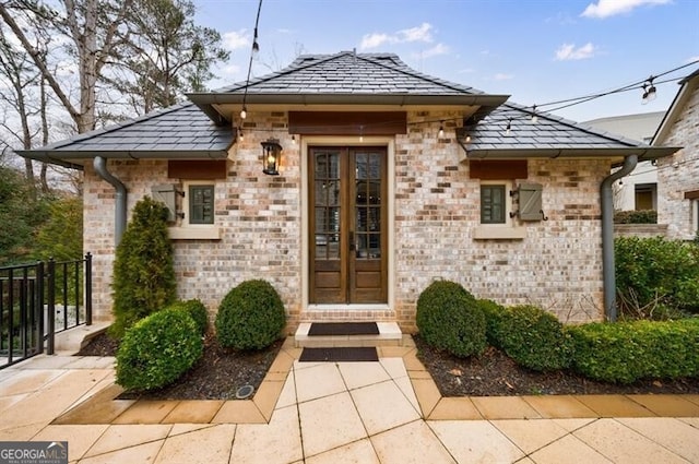 doorway to property featuring a high end roof, brick siding, and fence