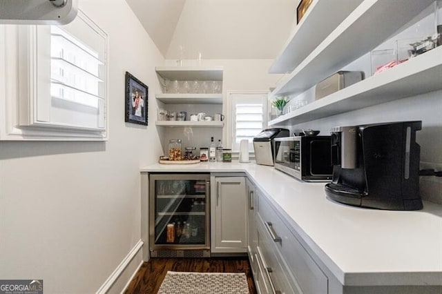 bar with a dry bar, dark wood finished floors, wine cooler, stainless steel microwave, and vaulted ceiling