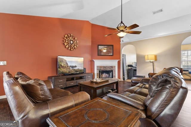 living area with visible vents, arched walkways, ceiling fan, vaulted ceiling, and a fireplace