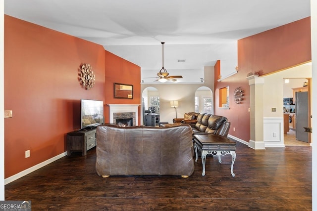 living room featuring arched walkways, vaulted ceiling, ceiling fan, a stone fireplace, and wood finished floors