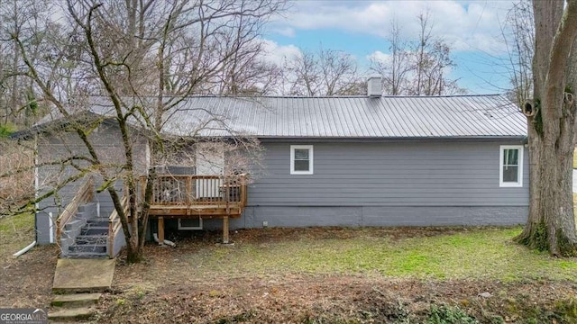 back of house featuring metal roof, a wooden deck, a chimney, and stairway