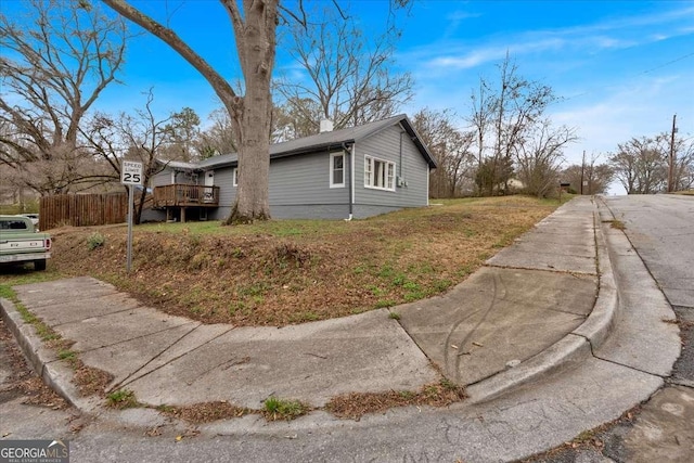 view of side of home with a wooden deck, a chimney, and fence