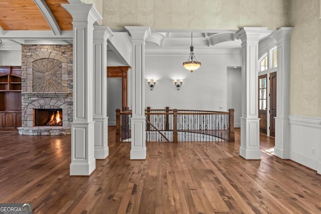 interior space with ornate columns, hardwood / wood-style floors, beamed ceiling, and a stone fireplace