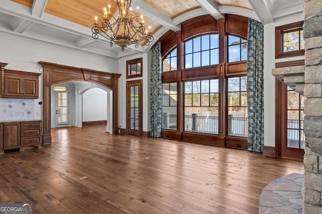 unfurnished living room featuring baseboards, arched walkways, dark wood finished floors, and beamed ceiling