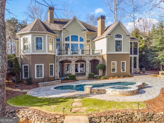 back of property featuring a chimney, stucco siding, a balcony, and an in ground hot tub