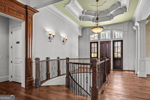 entrance foyer featuring ornamental molding, a raised ceiling, ornate columns, and hardwood / wood-style flooring